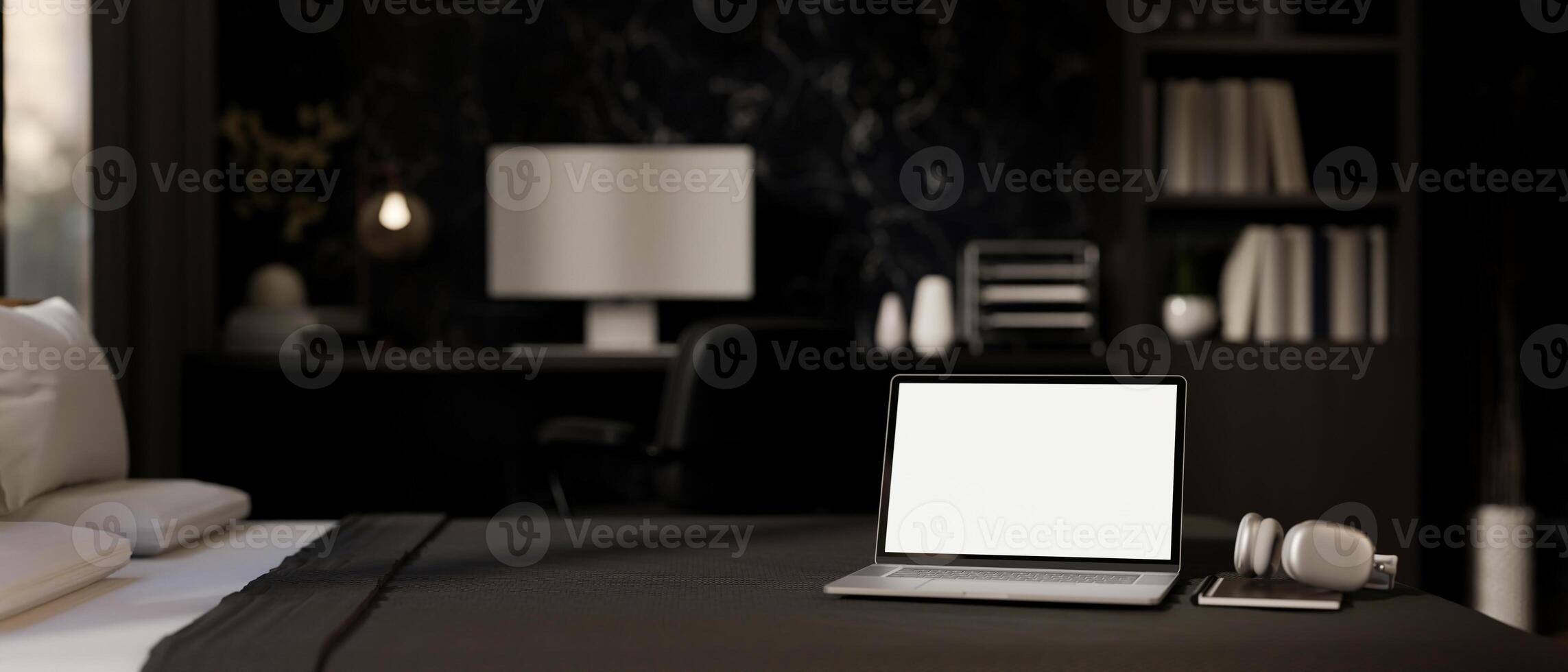 A white-screen laptop computer, a book, and a headphone on a bed in a modern black bedroom. photo