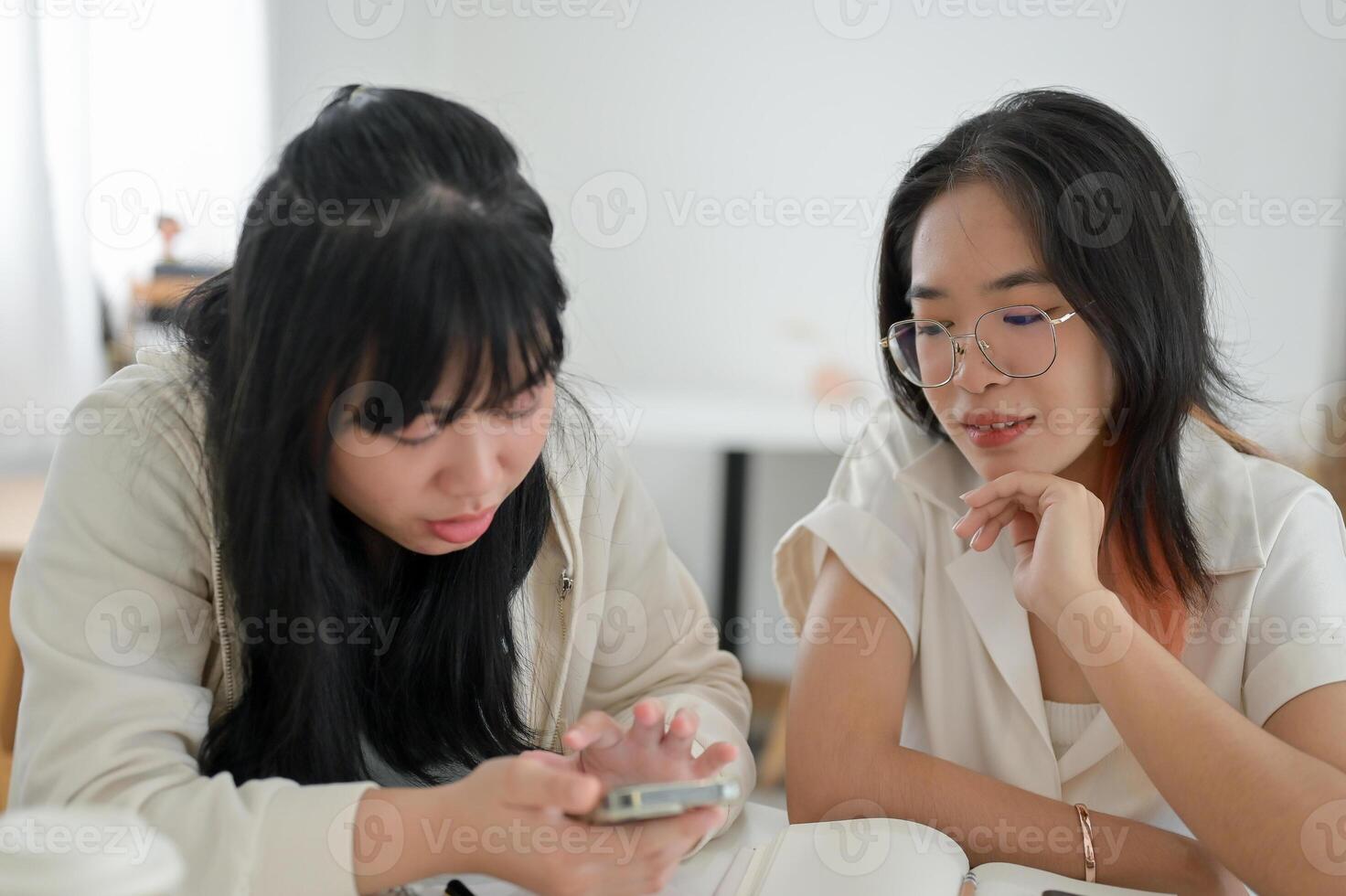 A young Asian woman is sitting with her friend in a cafe, studying or doing homework. photo