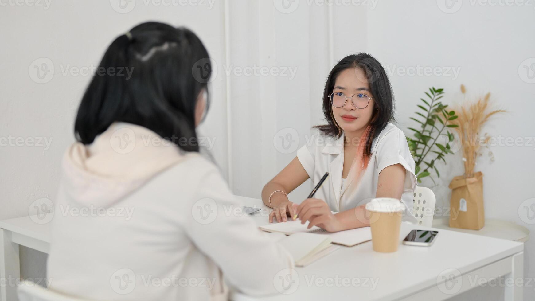 A young, friendly Asian female college student is helping her friend with math homework at a cafe. photo