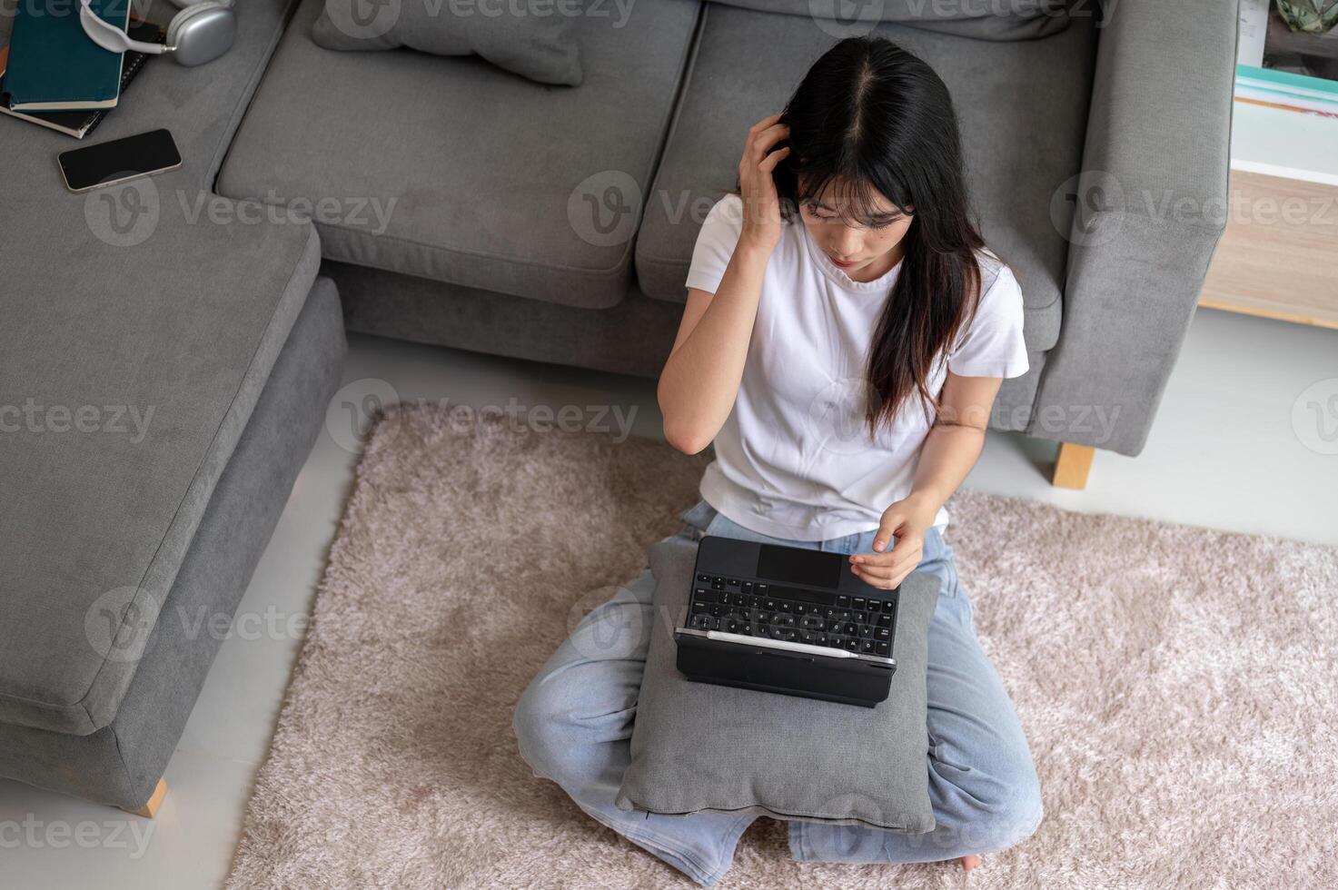 Top view image of an Asian woman sits on a carpet in the living room and uses her digital tablet. photo