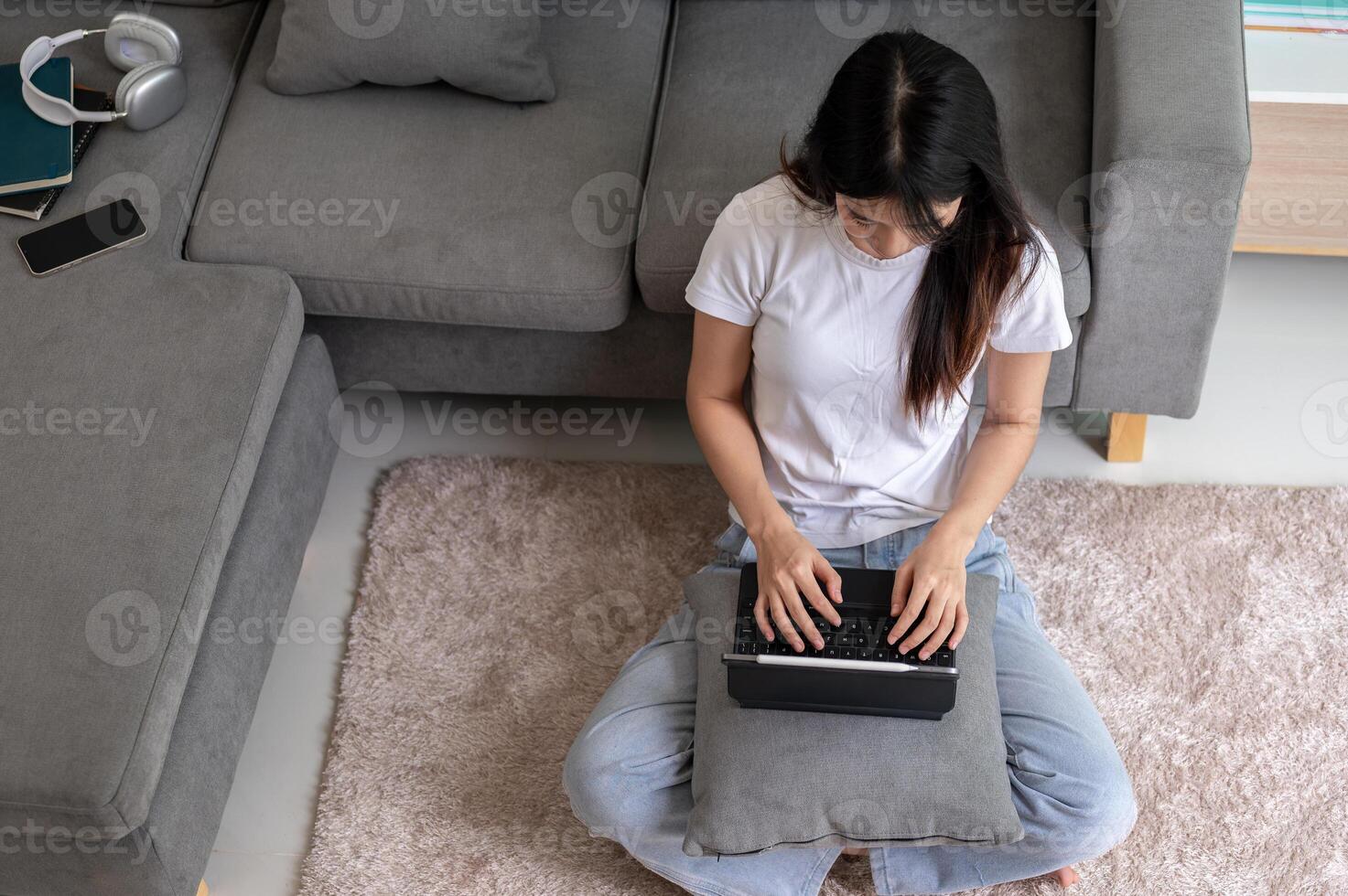 Top view image of an Asian woman sits on a carpet in the living room and uses her digital tablet. photo