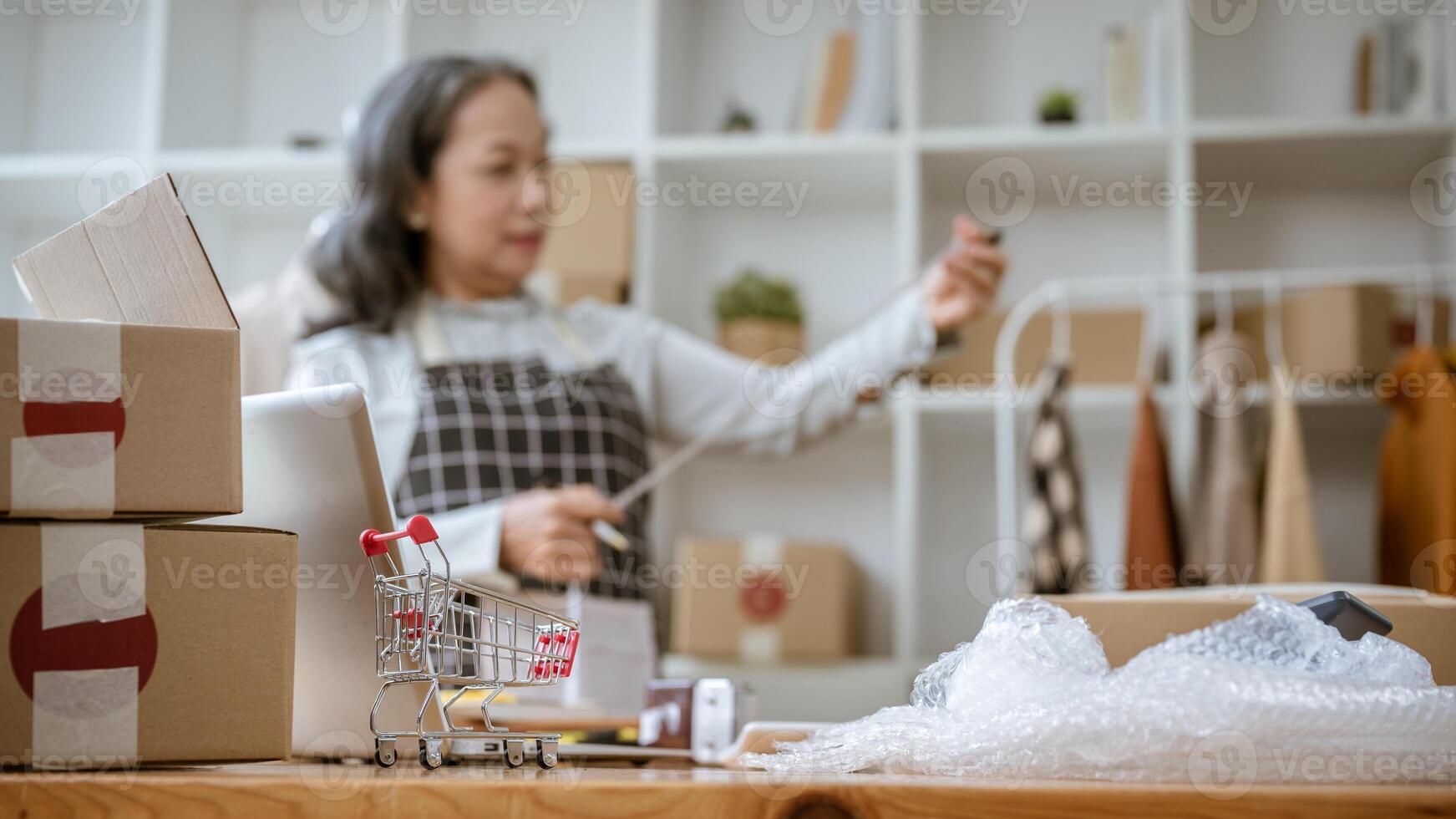 A shopping cart model, cardboard boxes, bubble wrap, computer, and equipment on a table. photo