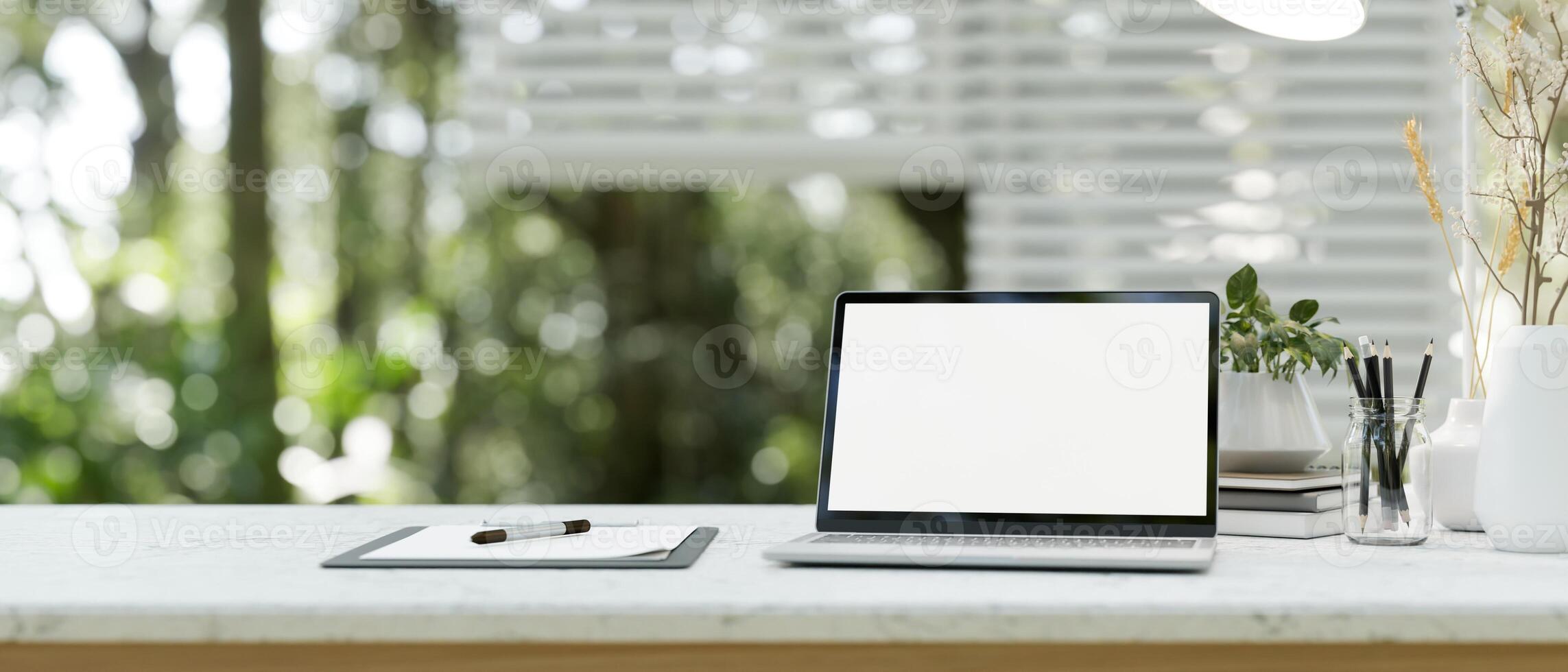 A close-up image of a laptop computer white-screen mockup on a white table in a modern office room. photo