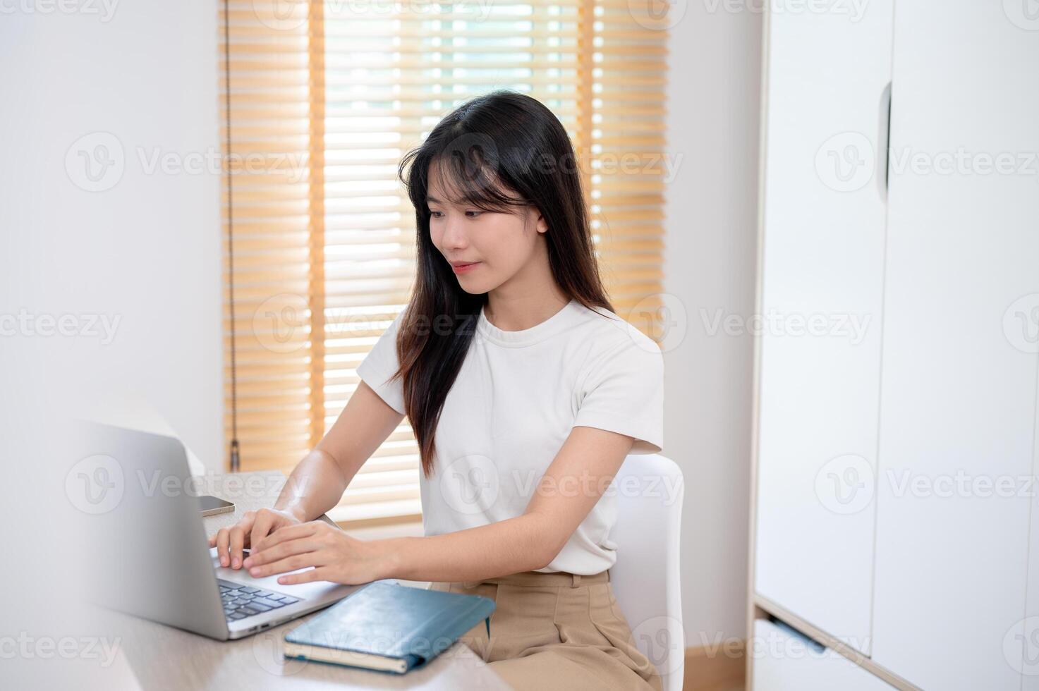A beautiful young Asian woman focusing on her work on computer, working remotely from home. photo