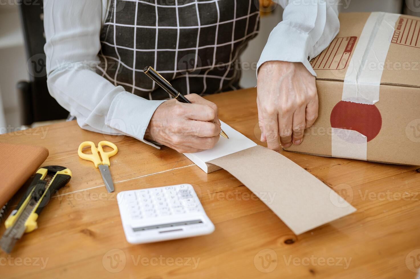 A cropped image of a mature female tailor taking notes in a notepad while working in her studio. photo