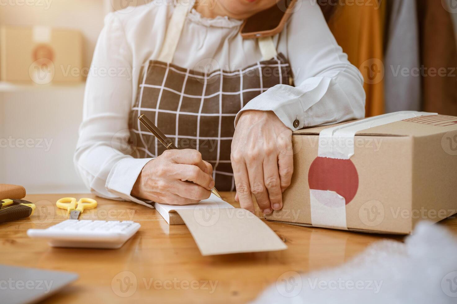 A cropped image of a mature female tailor taking notes in a notepad while working in her studio. photo