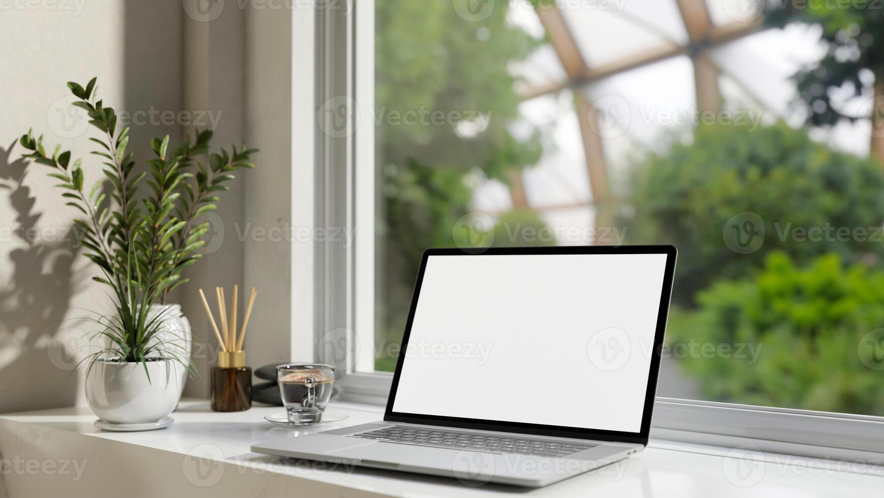 A laptop computer white-screen mockup on a white table against the window with a green nature view. photo