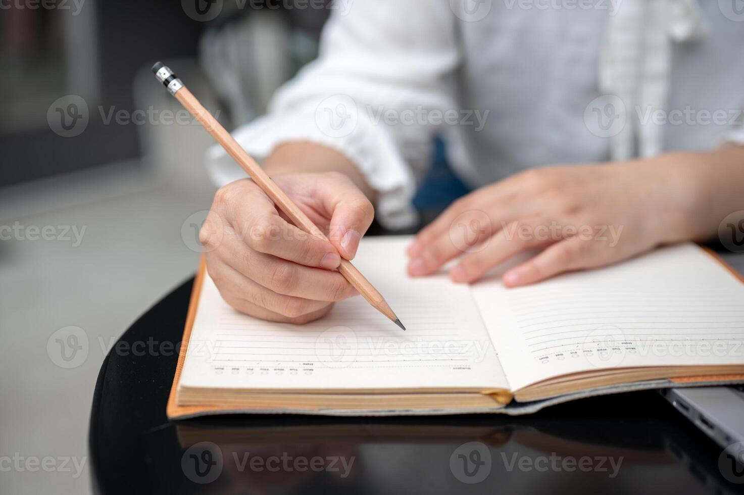 A close-up image of a woman sitting at a table, holding a pencil, and writing in a notebook. photo