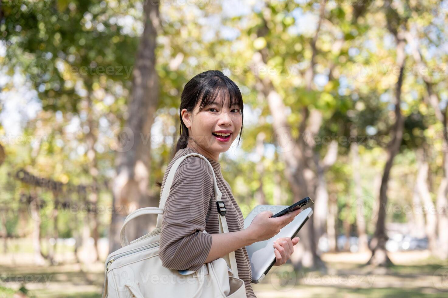 An attractive young Asian female college student with a backpack is walking in the campus park. photo