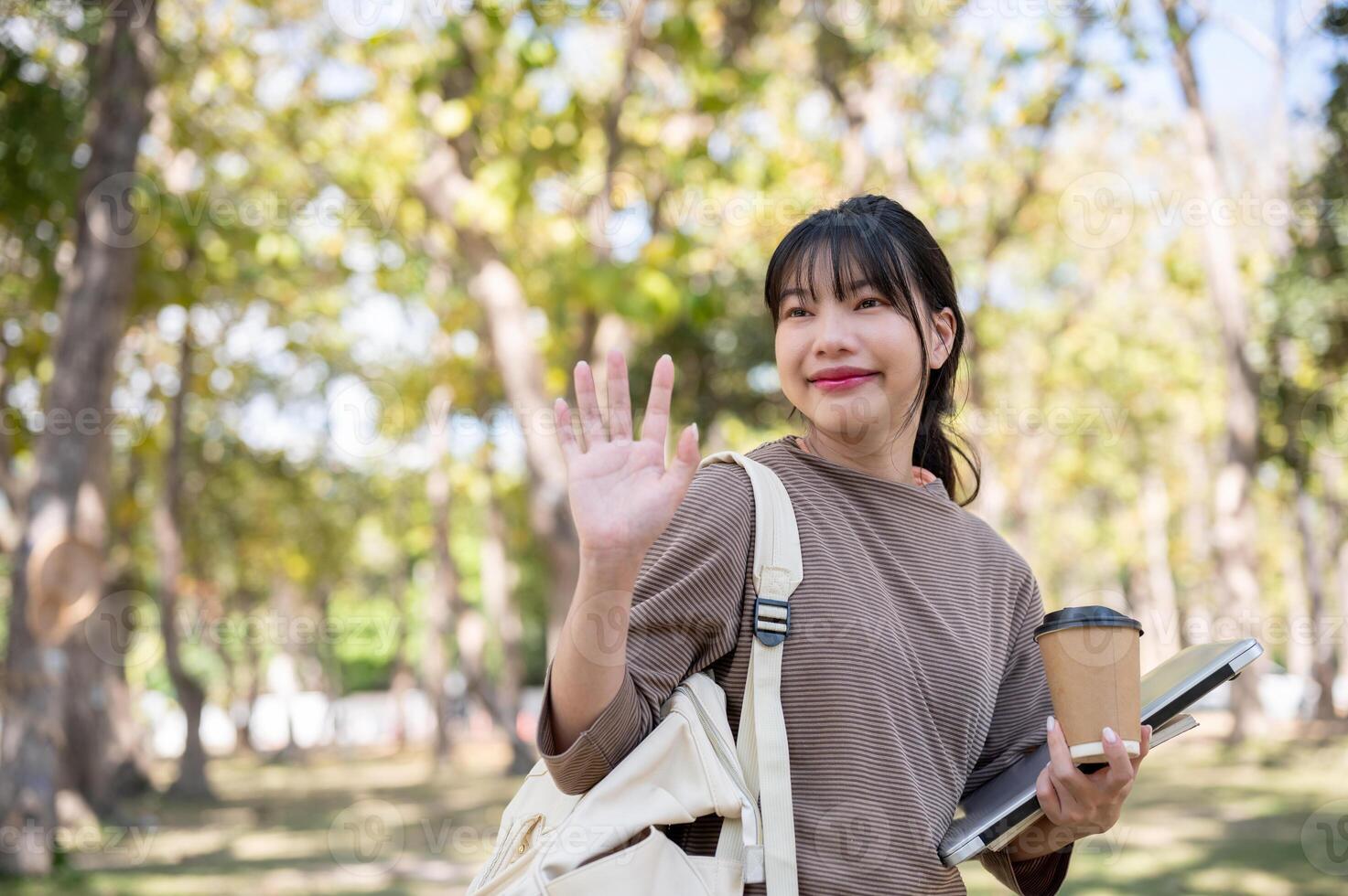 A friendly female student is waving her hand, greeting, or saying goodbye to her friend in a park. photo