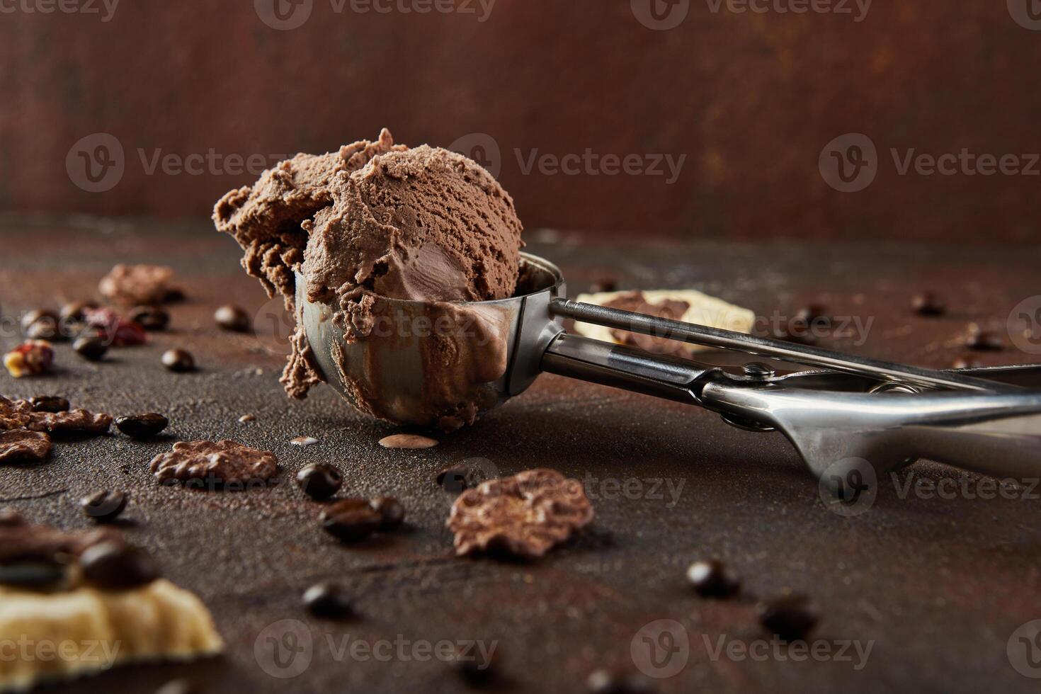 Chocolate ice cream in special metal spoon for rolling balls on brown concrete background photo