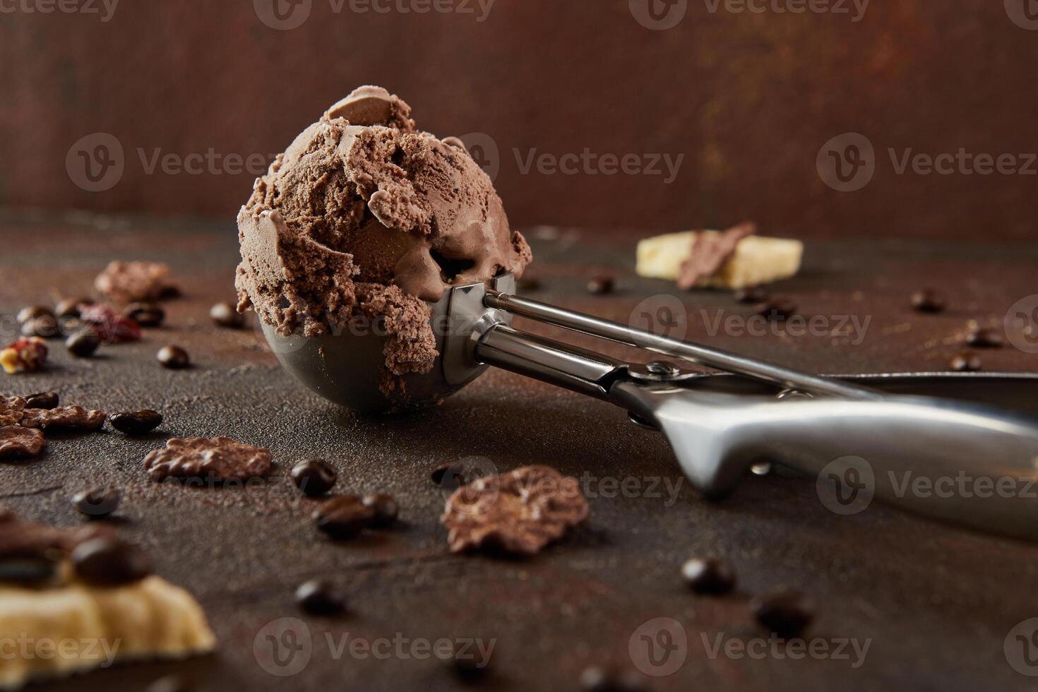 Chocolate ice cream in special metal spoon for rolling balls on brown concrete background photo