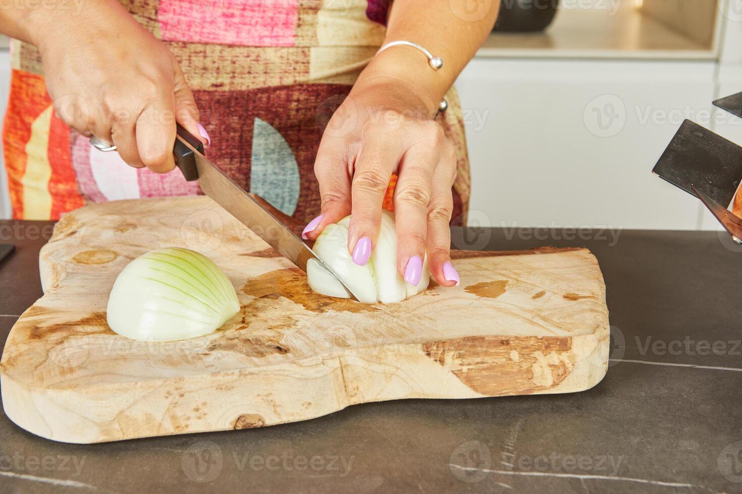 A woman chops onions on a wooden board in her home kitchen photo