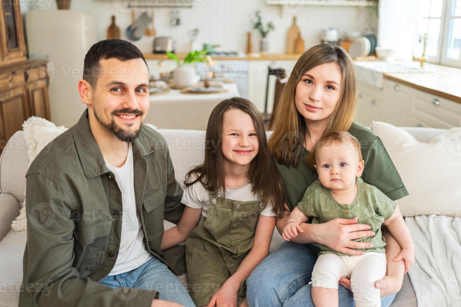 Happy family at home. Mother father two children daughters relaxing on sofa indoor. Mom dad parents baby girls kids relax playing having fun together. Family smiling laughing enjoying tender moment photo