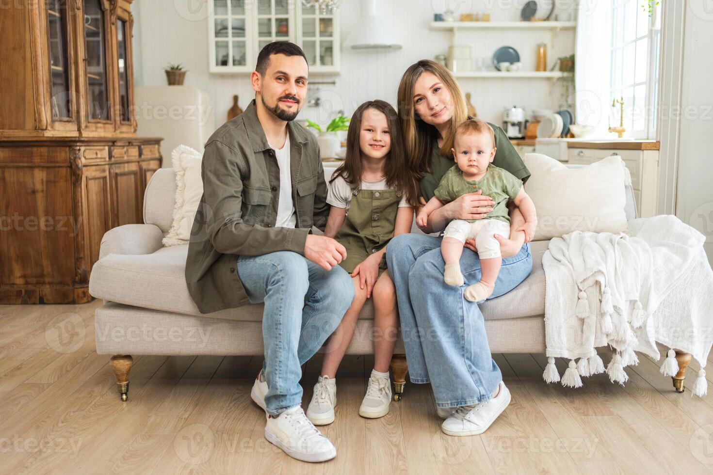 Happy family at home. Mother father two children daughters relaxing on sofa indoor. Mom dad parents baby girls kids relax playing having fun together. Family smiling laughing enjoying tender moment photo
