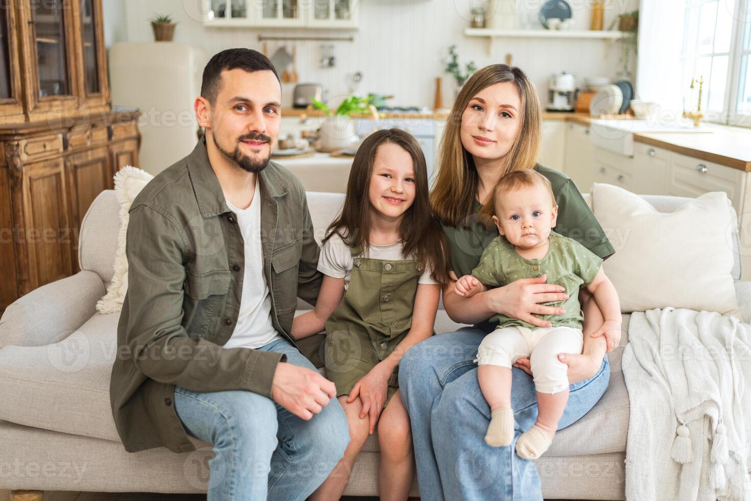contento familia a hogar. madre padre dos niños hijas relajante en sofá interior. mamá papá padres bebé muchachas niños relajarse jugando teniendo divertido juntos. familia sonriente riendo disfrutando oferta momento foto