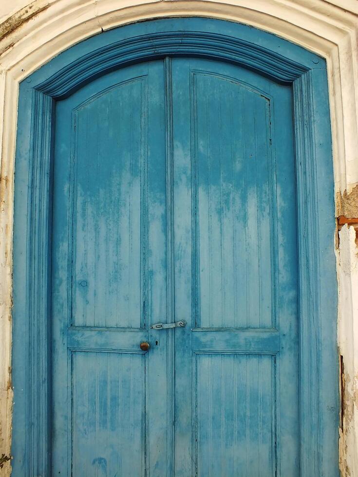 ancient and antique blue wooden javanese door with cracking old wall around it photo