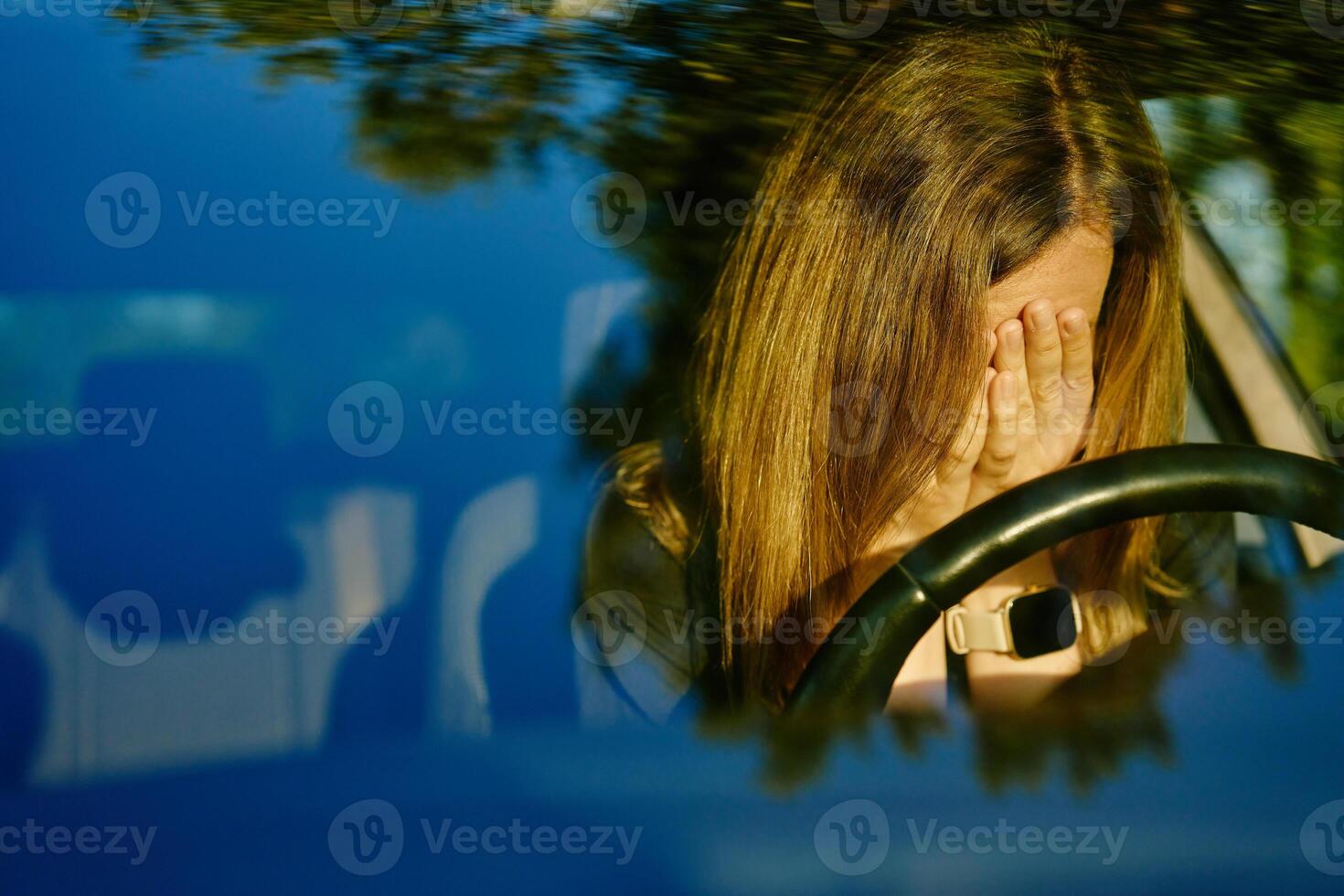 Woman is seated inside car with her head resting on steering wheel photo