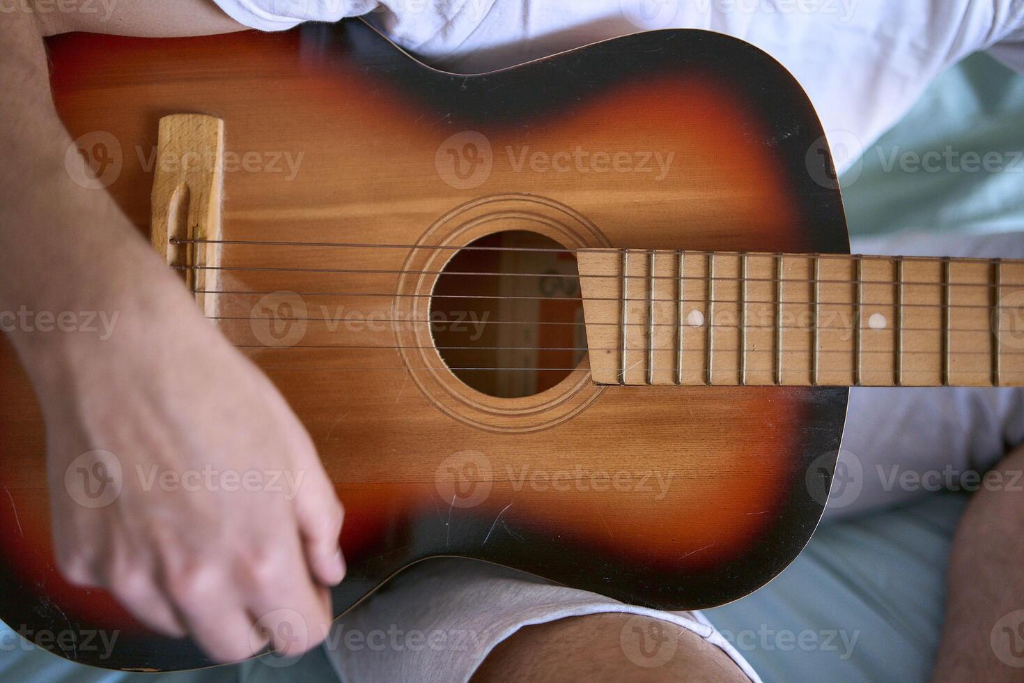 a young man is learning to play the guitar at home, a cat is lying next to him and listening photo