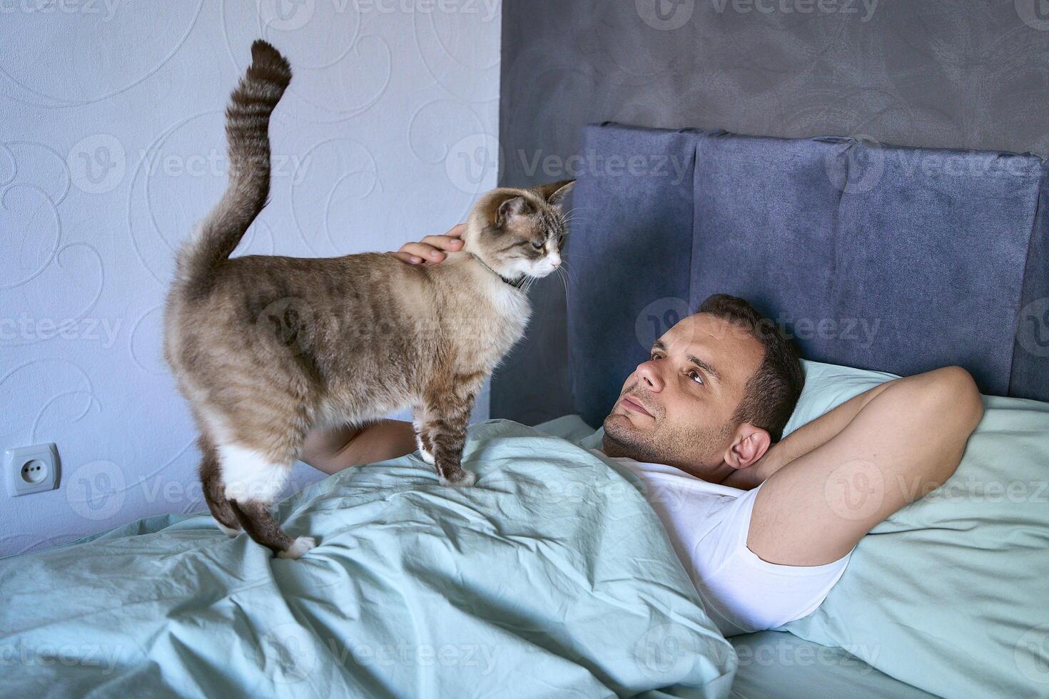 a young man sleeping with a cat on his chest, morning routine photo