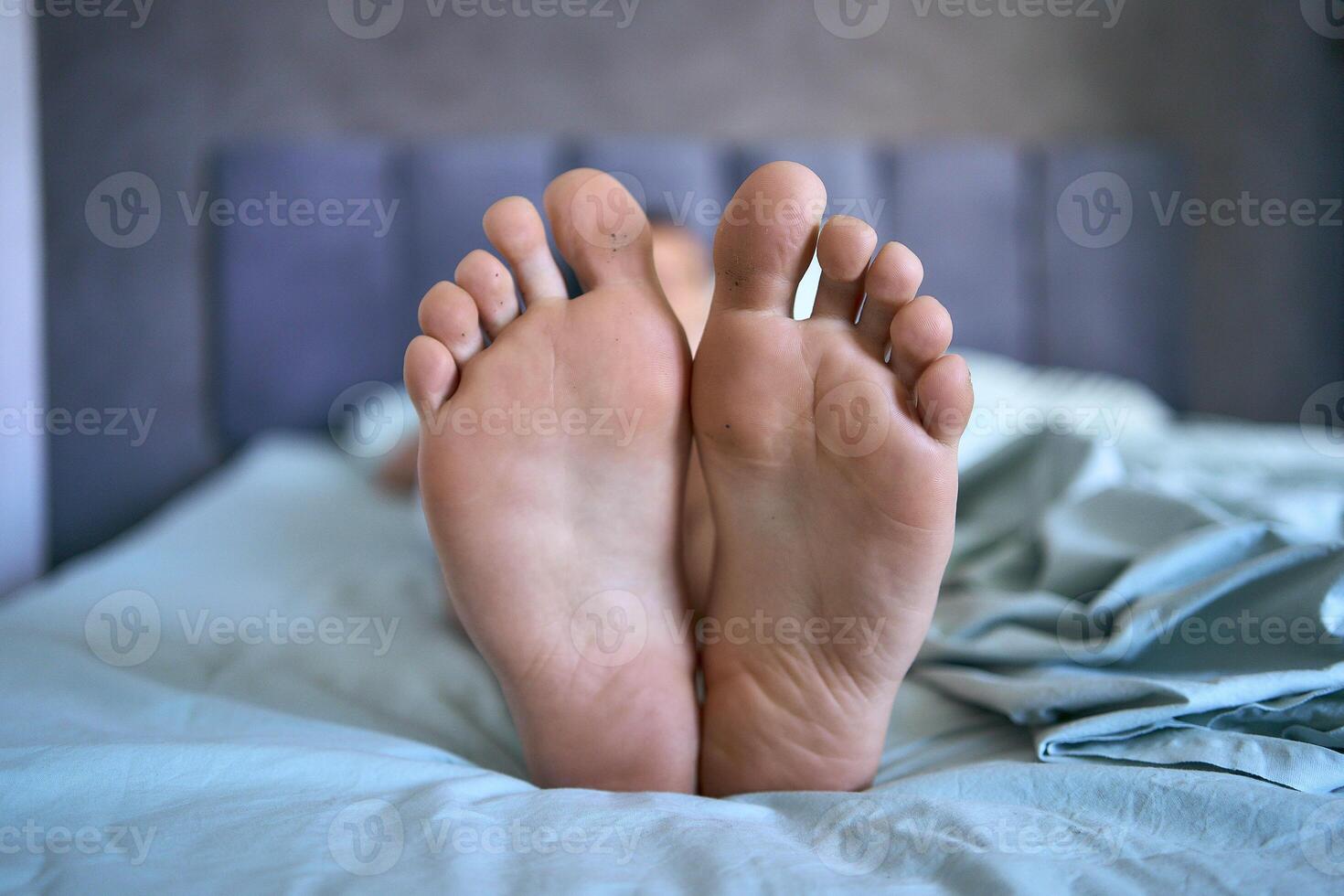 man is lying on a bed, big feet on the bed photo