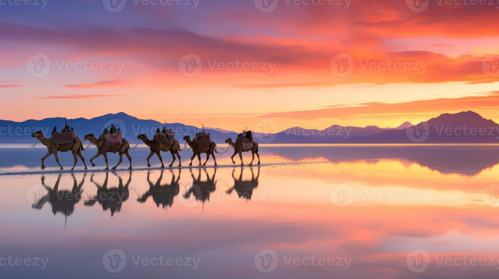 Silhouette of a camel caravan walking along a beach at sunset, with reflection on water photo
