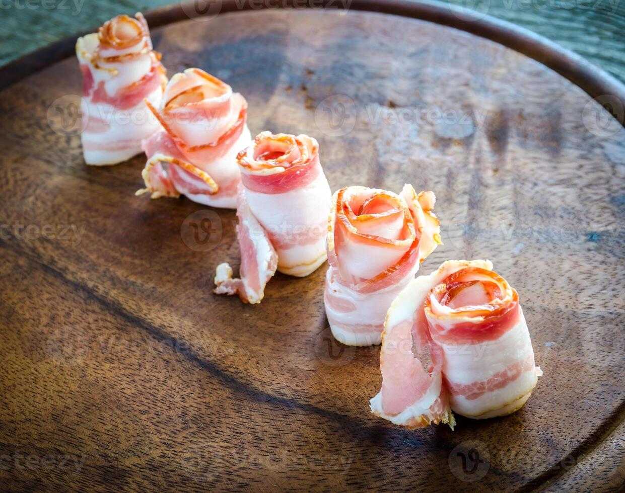 Rolled bacon strips on wooden board photo