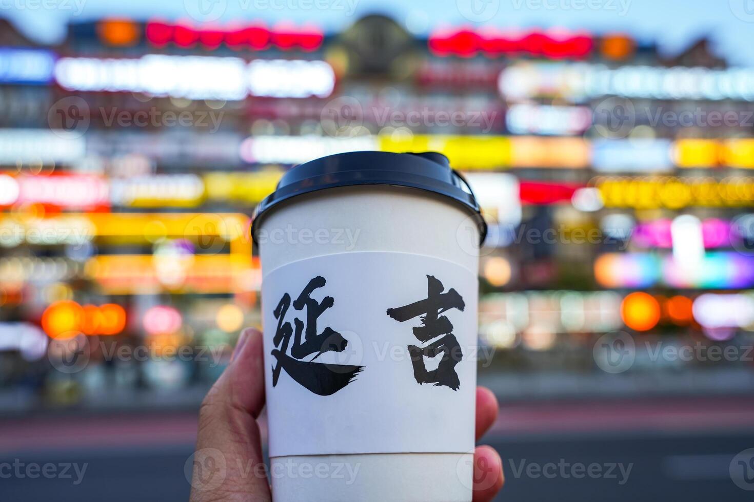 Hand holding cup wirh blur building on background, chinese alphabet means YANJI city in China. photo