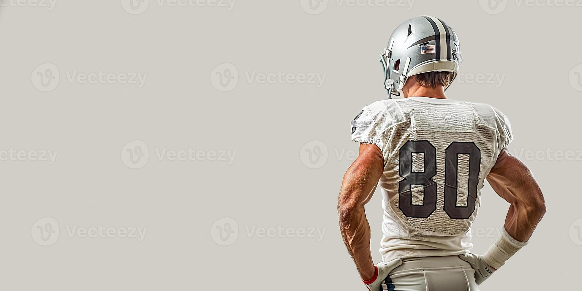 American football player in a gray helmet and white uniform stands with his back and holds his hands on his sides photo