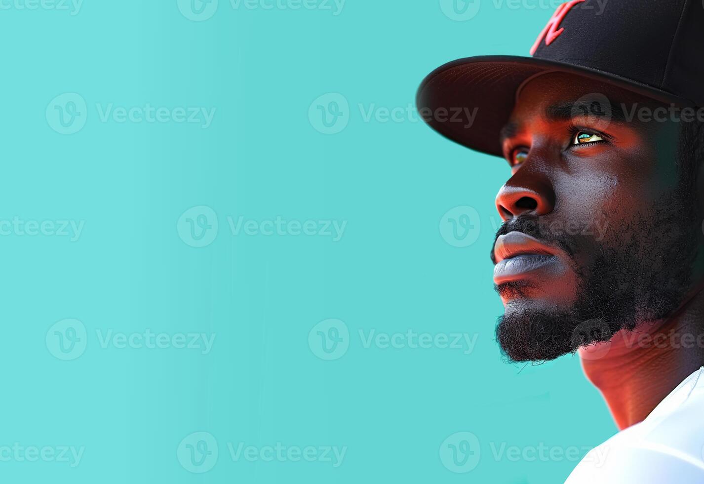 A black baseball player with a beard and mustache in a black cap looks up against a green background photo
