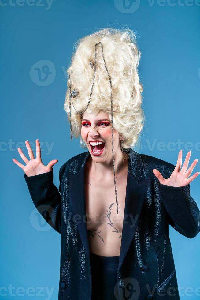 Funny angry woman in royale wig and jacket screaming in blue studio photo