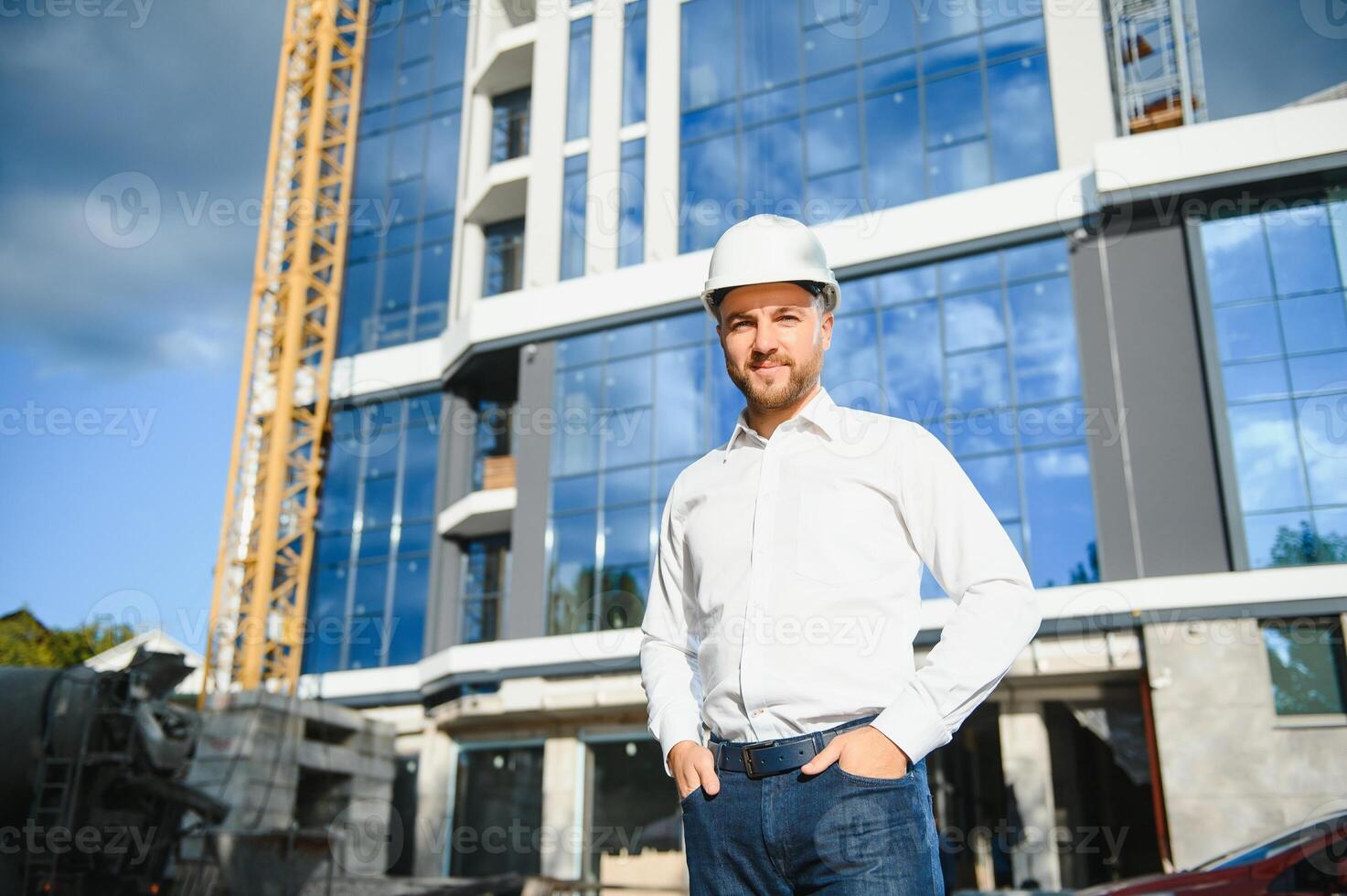 Successful engineer or architect, crane and building construction at backgrpound. Joyous businessman wearing helmet photo