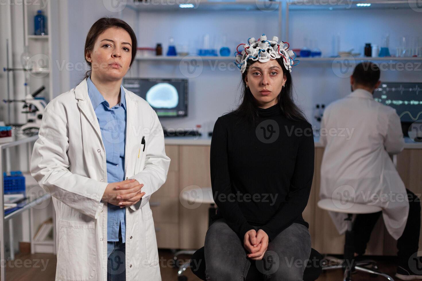 Portrait of neurologist doctor standing beside woman patient with medical eeg headset during neuroscience experiment in medical laboratory. Team of researcher analyzing brain activity evolution photo