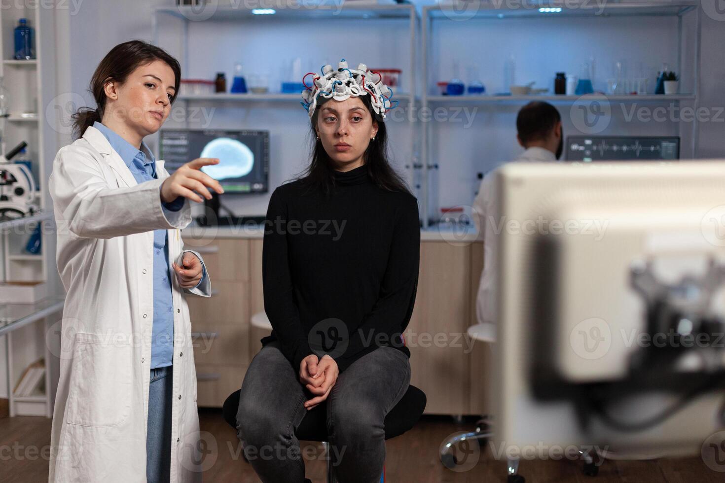 Neurologist doctor showing monitor with brain activity to woman patient with eeg scanner on head during neuroscience experiment in medical lab. Scientist physician analyzing nervous system evolution photo