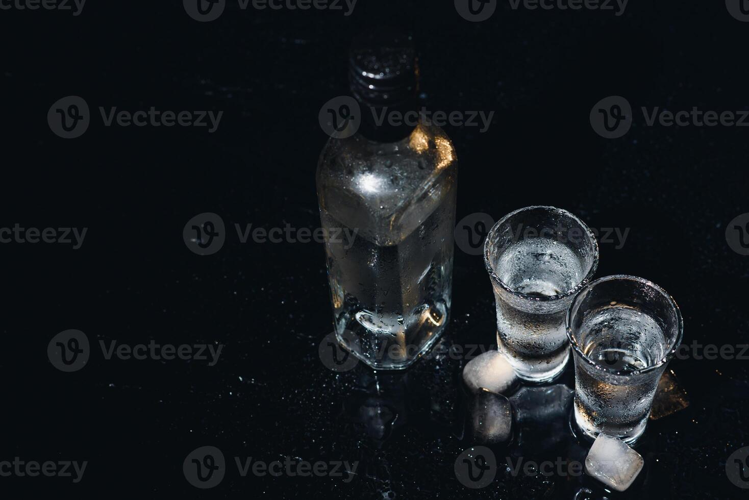 Vodka in shot glasses on black background, iced strong drink in misted glass. photo