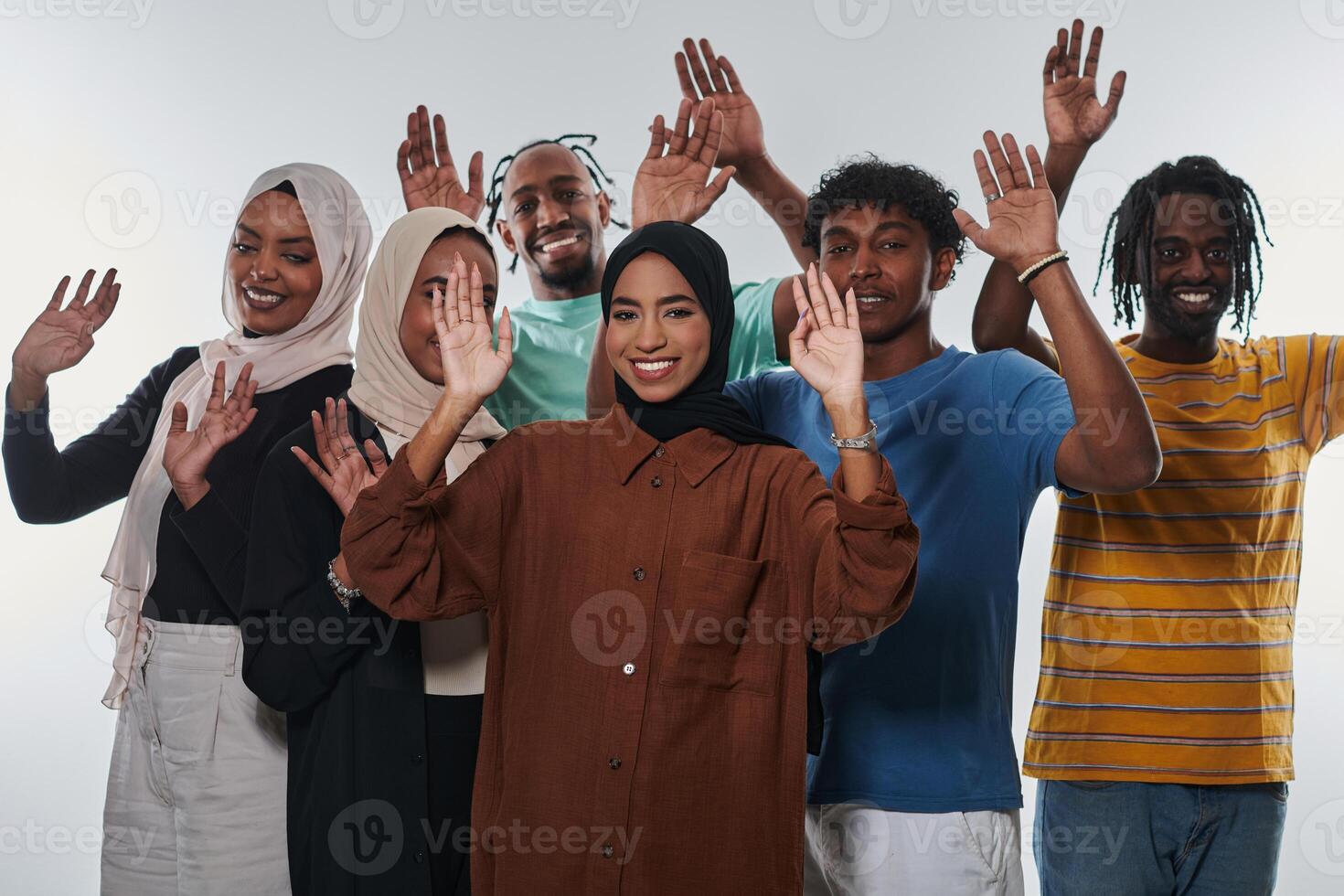 A jubilant and diverse group, including an African American man and hijab-wearing girls, exuberantly wave and celebrate, embodying the vibrancy of student life against a white backdrop, symbolizing photo
