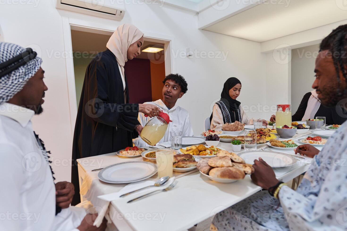 In the sacred month of Ramadan, a Muslim family joyously comes together around a table, eagerly awaiting the communal iftar, engaging in the preparation of a shared meal, and uniting in anticipation photo