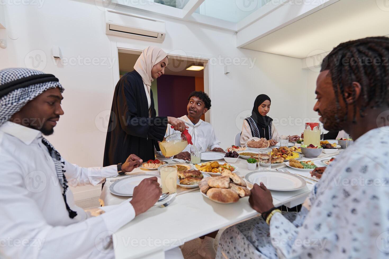 In the sacred month of Ramadan, a Muslim family joyously comes together around a table, eagerly awaiting the communal iftar, engaging in the preparation of a shared meal, and uniting in anticipation photo