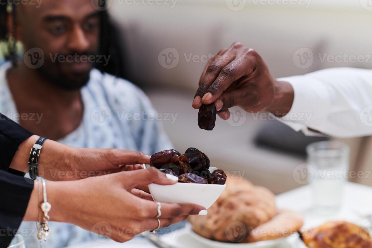 African American Muslim man delicately takes dates to break his fast during the Ramadan month, seated at the family dinner table, embodying a scene of spiritual reflection, cultural tradition, and the photo