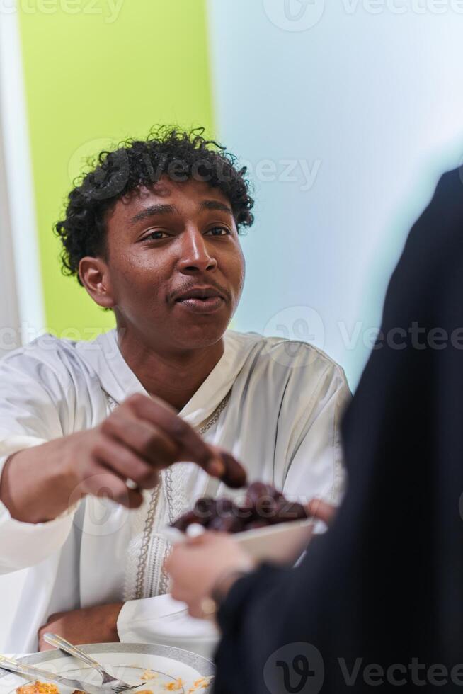 African American Muslim man delicately takes dates to break his fast during the Ramadan month, seated at the family dinner table, embodying a scene of spiritual reflection, cultural tradition, and the photo
