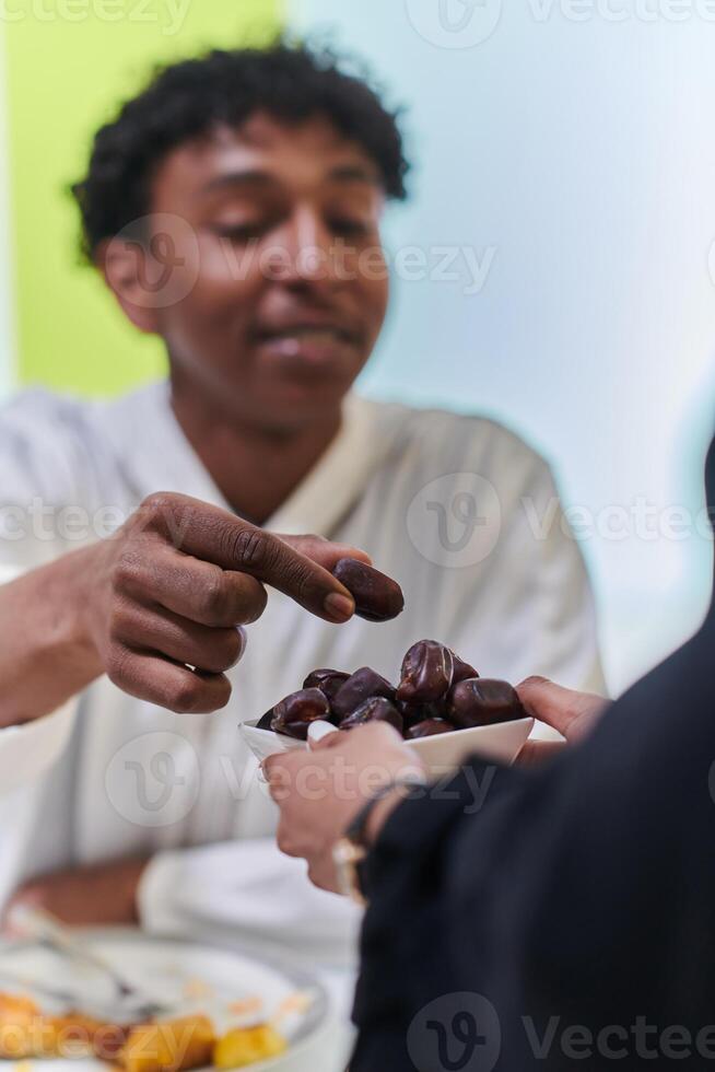 African American Muslim man delicately takes dates to break his fast during the Ramadan month, seated at the family dinner table, embodying a scene of spiritual reflection, cultural tradition, and the photo