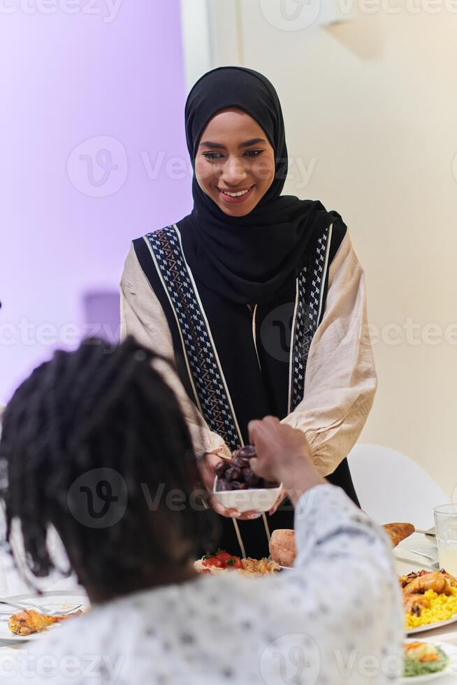 In a heartwarming scene during the sacred month of Ramadan, a traditional Muslim woman offers dates to her family gathered around the table, exemplifying the spirit of unity, generosity, and cultural photo