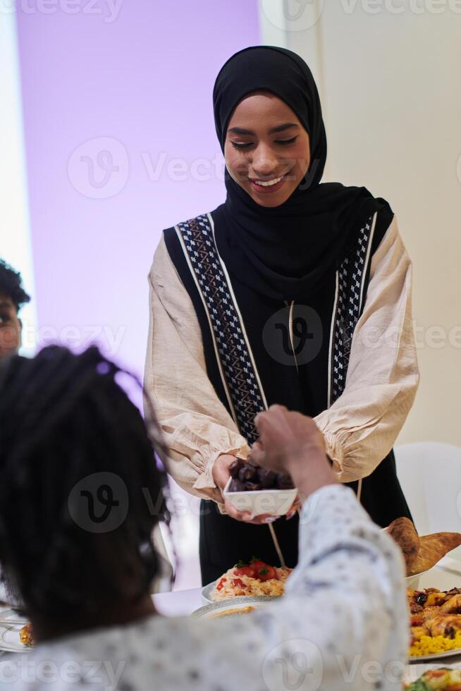 In a heartwarming scene during the sacred month of Ramadan, a traditional Muslim woman offers dates to her family gathered around the table, exemplifying the spirit of unity, generosity, and cultural photo