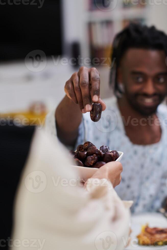 African American Muslim man delicately takes dates to break his fast during the Ramadan month, seated at the family dinner table, embodying a scene of spiritual reflection, cultural tradition, and the photo