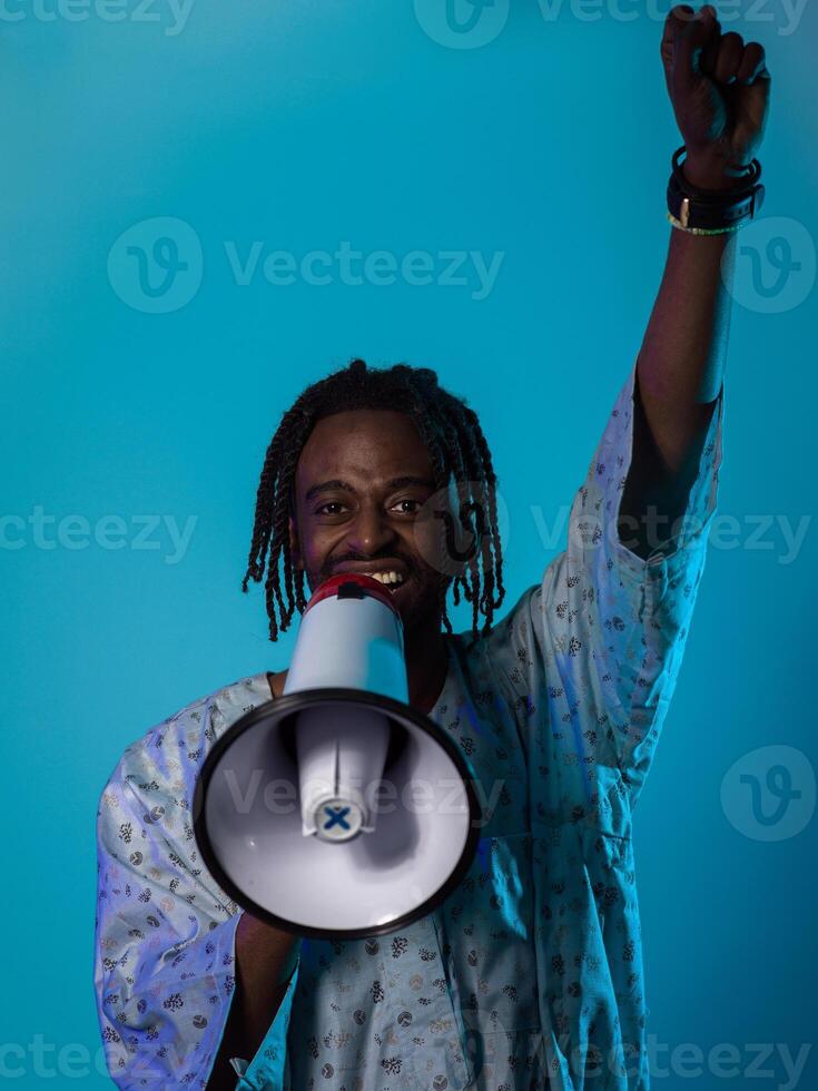 In a powerful and symbolic image, an African American man wears traditional clothing, passionately wields a megaphone against a striking blue background, with his hand raised in the air symbolizing photo