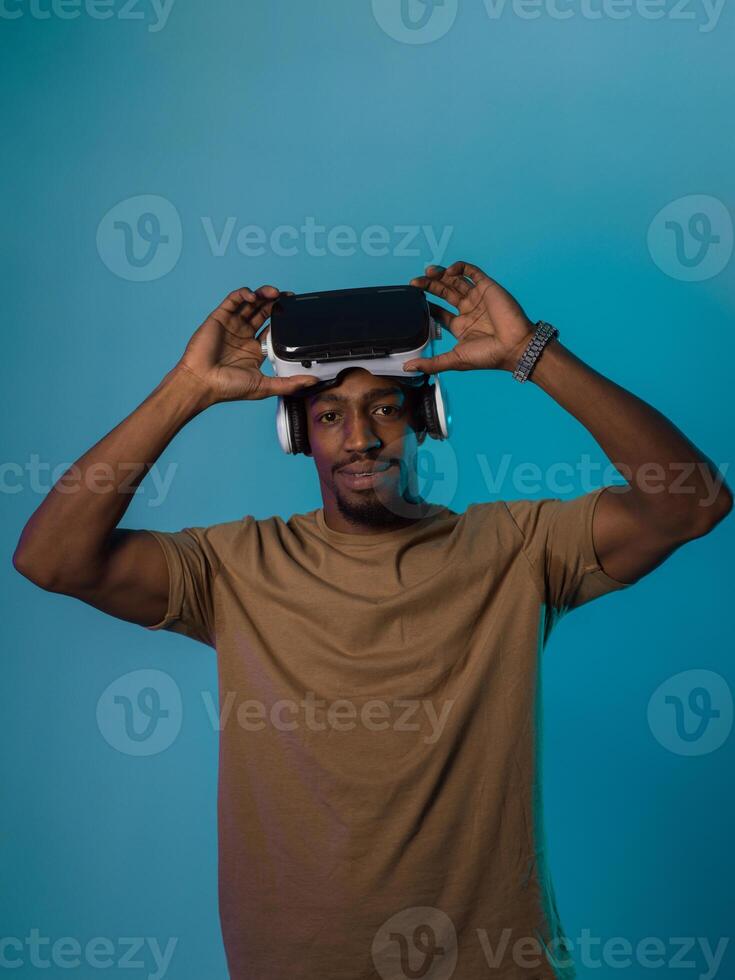 In a futuristic visual, an African American man stands isolated against a striking blue backdrop, adorned with VR glasses that transport him into a cutting-edge virtual reality experience, merging photo