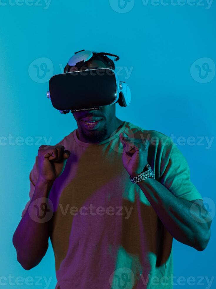 African American man immerses himself in a thrilling horror gaming experience using VR glasses, creating an isolated and intense atmosphere against a striking blue background photo