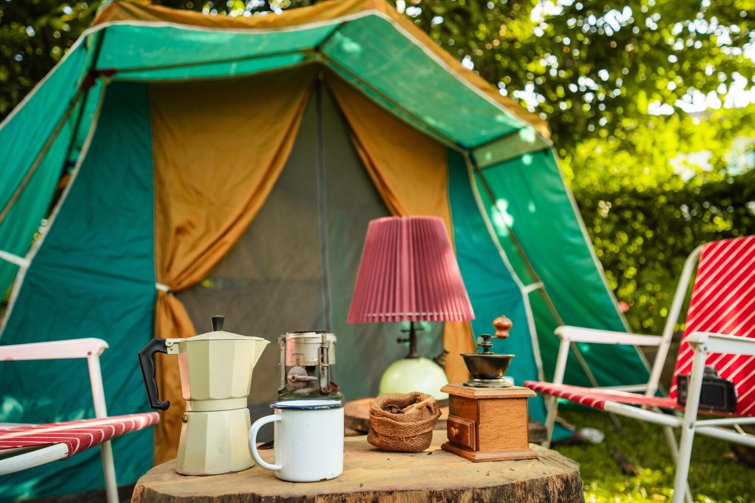 selective focus of vintage coffee set on the old wooden table In front of the retro cabin tent, Antique oil lamp, retro chairs, Group of camping tents, and soft focus. photo