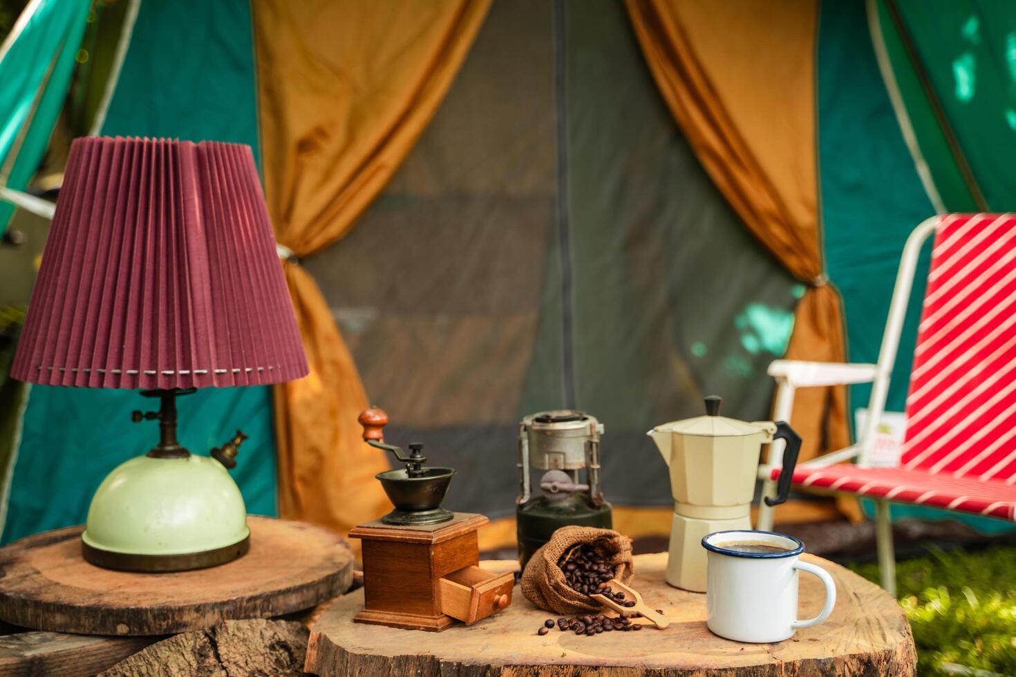 selective focus of vintage coffee set on the old wooden table In front of the retro cabin tent, Antique oil lamp, retro chairs, Group of camping tents, and soft focus. photo