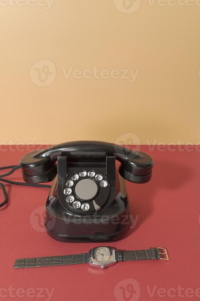 Retro phone from 60s 70s and retro watch with leather strap. On a red-orange background photo